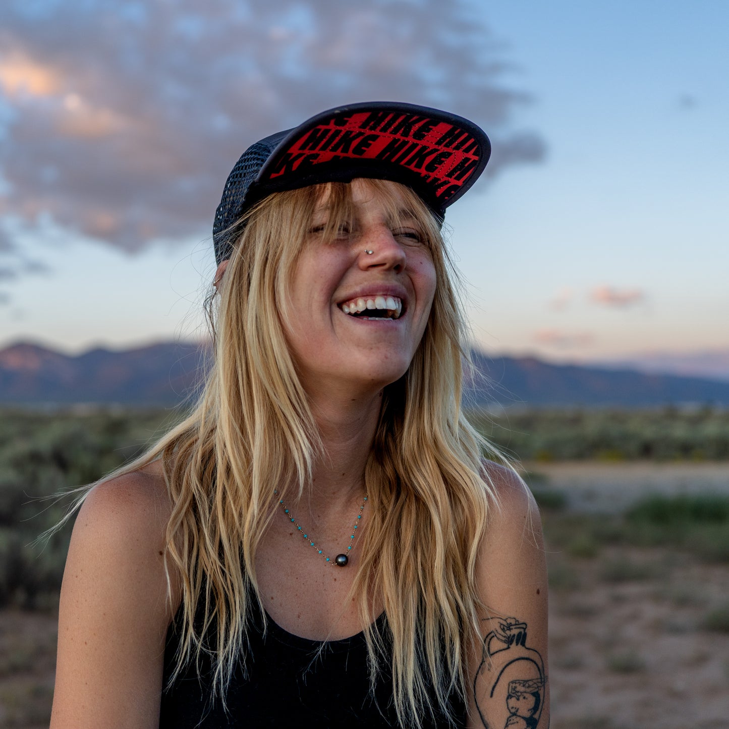 Woman wearing a cap with the word "HIKE" in red text in a desert landscape